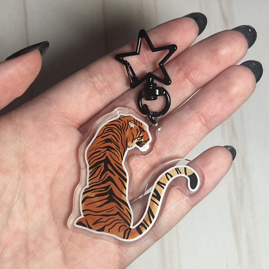 A video of a tiger shaped keychain with a star shaped clip being held in hands. The protective film of the keychain is removed.