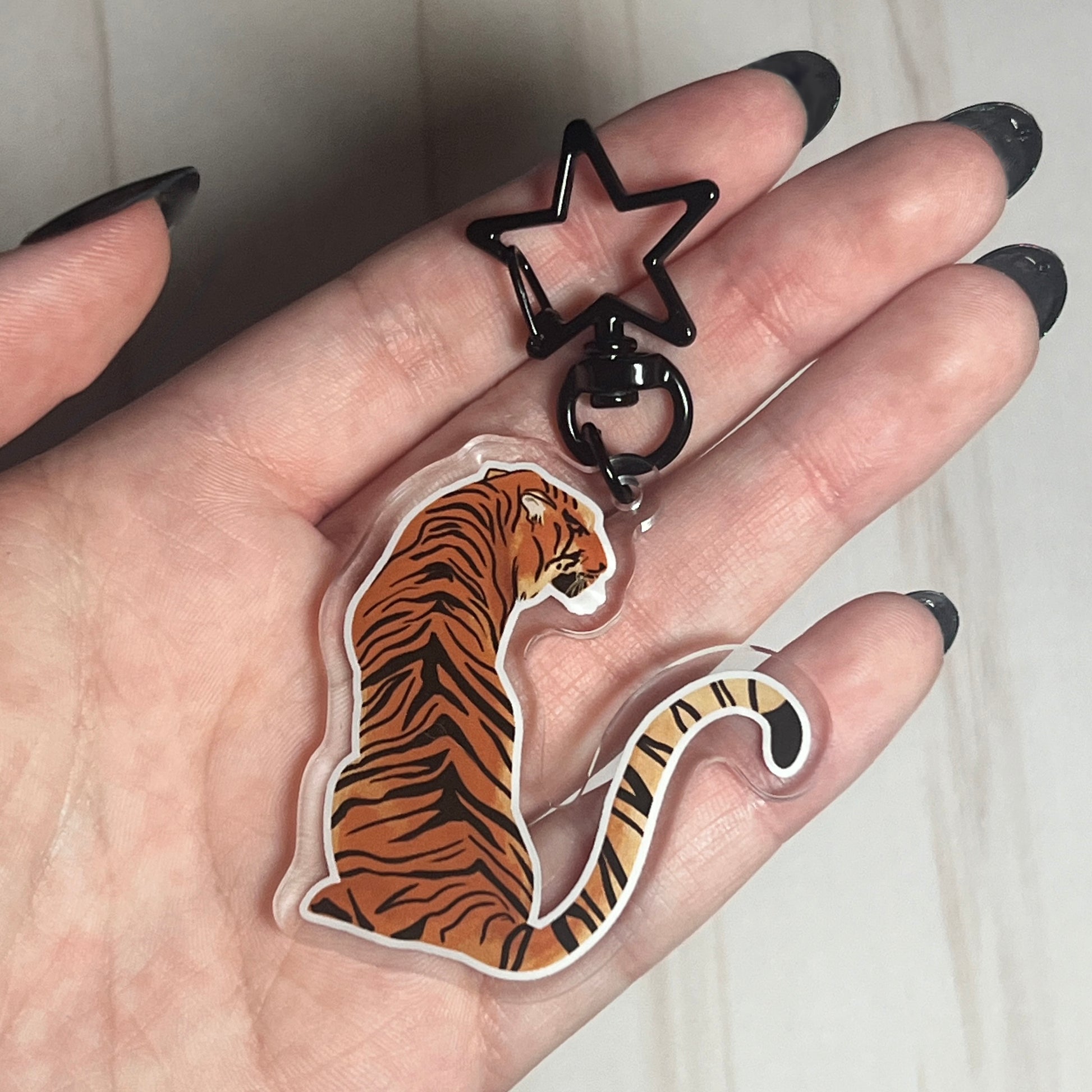 A video of a tiger shaped keychain with a star shaped clip being held in hands. The protective film of the keychain is removed.